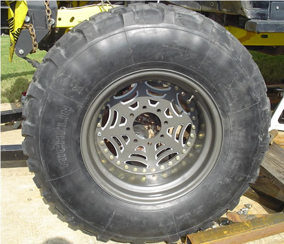 Large Michelin military-style tire on a gray beadlock wheel propped on a trailer