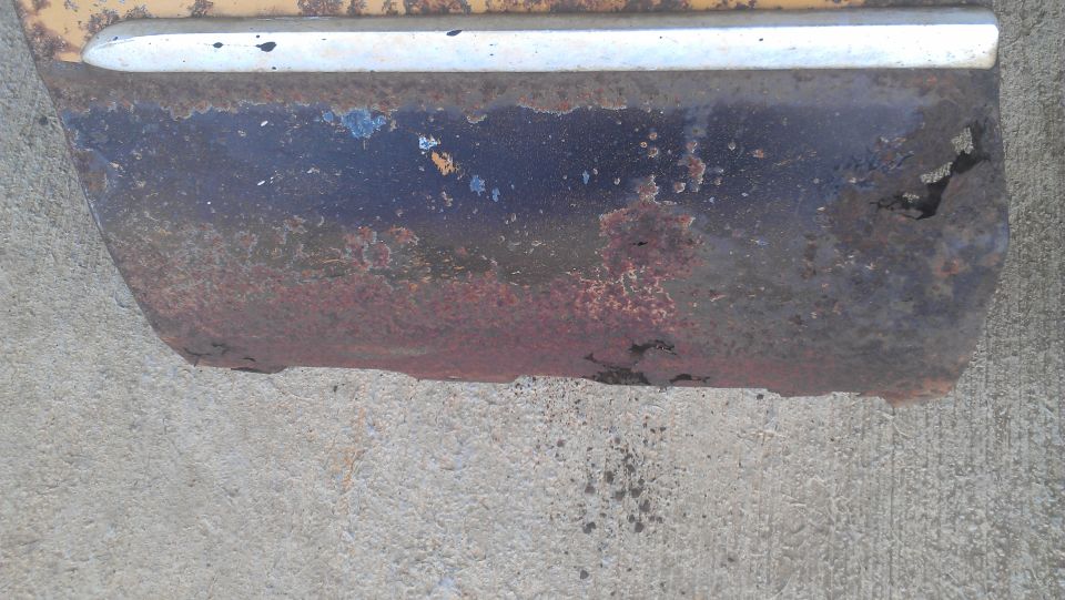 Close-up of a heavily rusted car lower body panel with a chrome trim piece above it