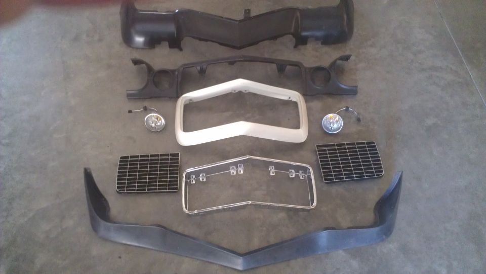 Car parts including bumpers, grille, and lights laid out on a concrete floor