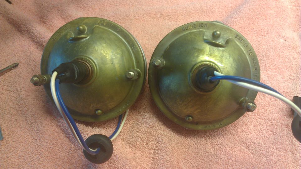 Two brass-colored headlights with blue and white wires attached, resting on a pink cloth