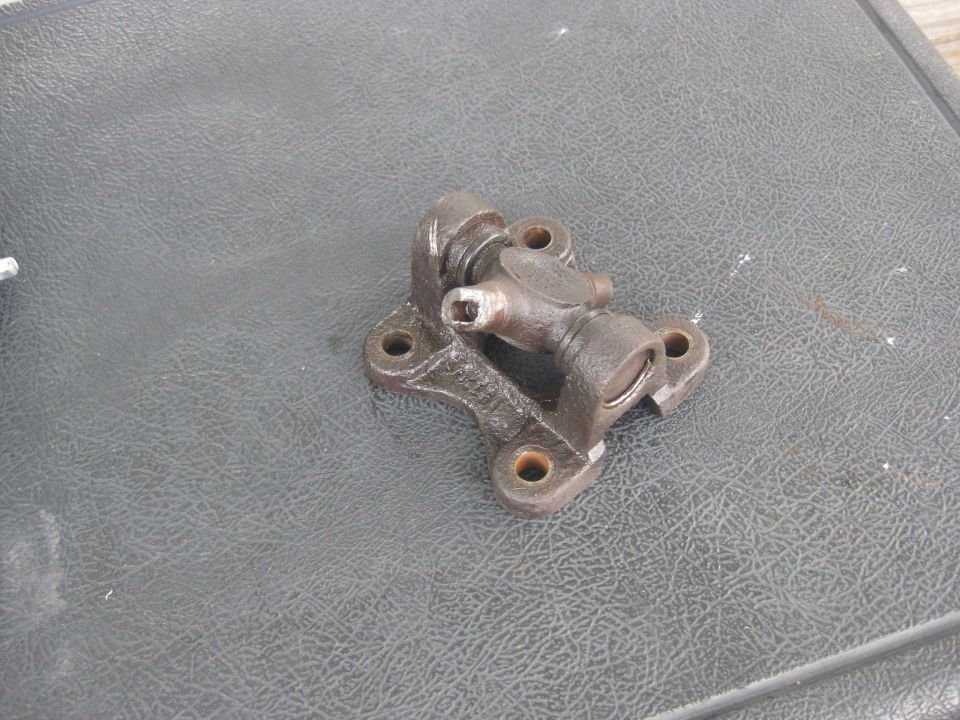 Metal universal joint part with four mounting holes on a textured dark surface