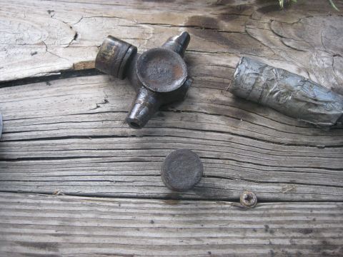 1994 Ford Bronco - A close-up view of a universal joint and a section of a driveshaft resting on weathered wooden planks.