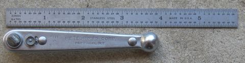 2000 Ford Crown Victoria - A metal ratchet wrench is shown next to a stainless steel ruler with inch and millimeter markings.
