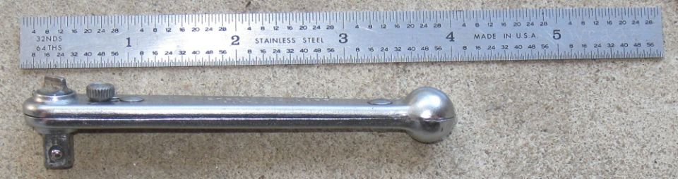 Ratchet wrench next to a ruler showing inches and millimeters