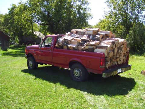 1987 Ford F-250 - A red 1987 Ford F-250 pickup truck is filled with cut firewood and parked on a grassy lawn.