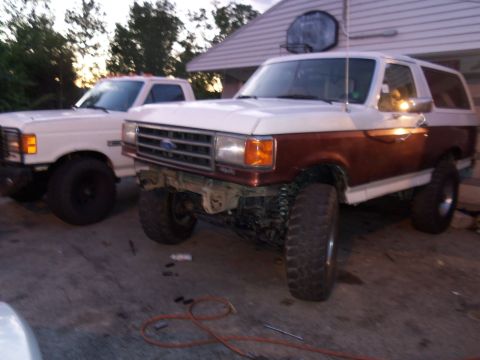 1989 Ford Bronco - This lifted 1989 Ford Bronco is parked next to a white pickup truck.