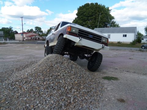1989 Ford Bronco - This modified Ford Bronco is shown with its front tires on a mound of gravel, highlighting its off-road capabilities.