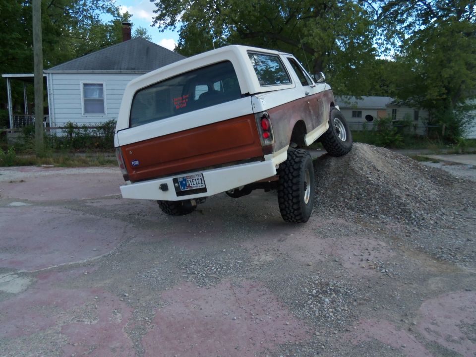 Two-tone brown and white Ford Bronco with lifted suspension driving up a gravel pile