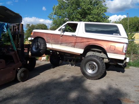 1989 Ford Bronco - A 1989 Ford Bronco is being lifted by a forklift, revealing its lifted suspension and off-road tires.