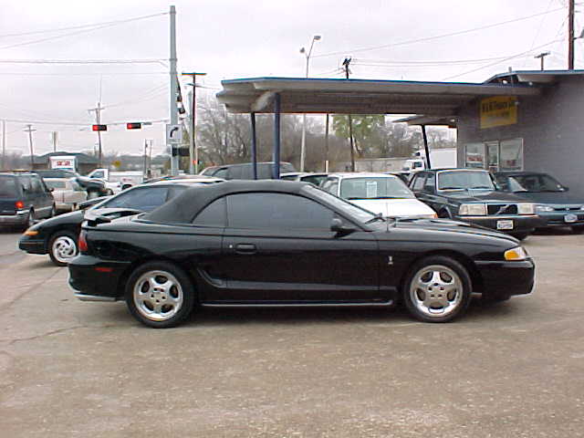 Black Mustang convertible, top up, side view in a car dealership lot