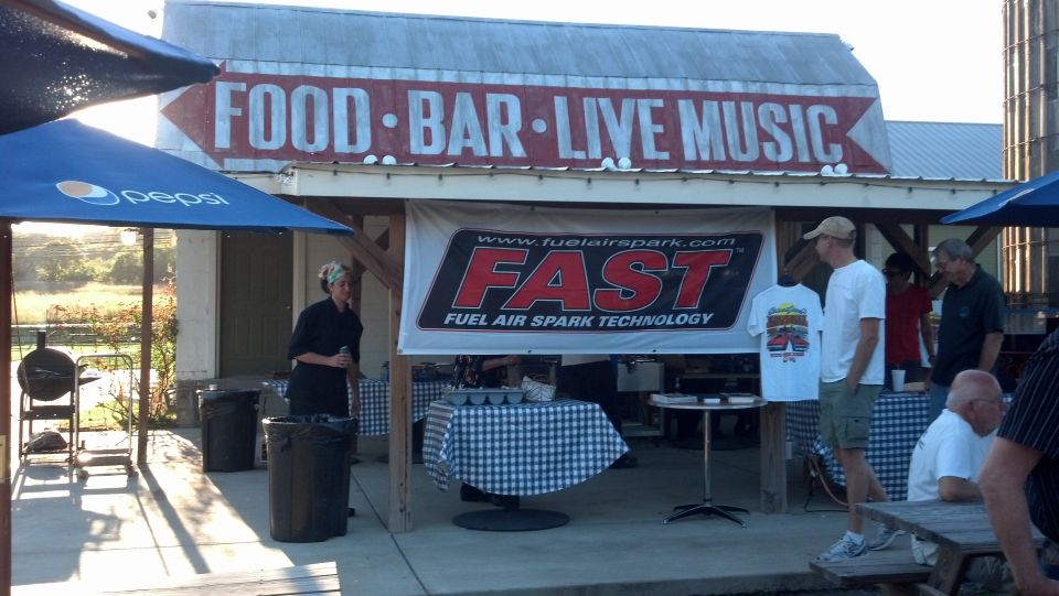 Outdoor event with a building sign reading 'FOOD BAR LIVE MUSIC' and a banner for FAST Fuel Air Spark Technology
