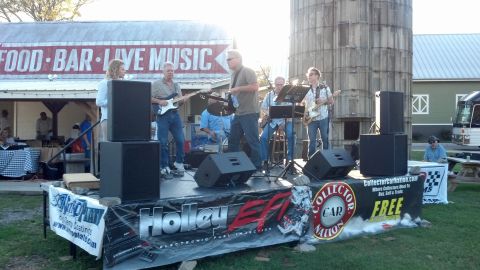 2007 Ford Mustang - A band plays live music on a stage set up outdoors, with a large silo visible behind them.