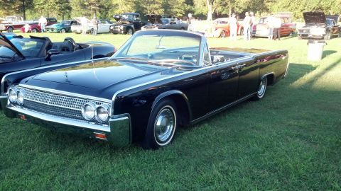 2007 Ford Mustang - A black 1961 Lincoln Continental convertible is displayed at a car show with other vehicles in the background.