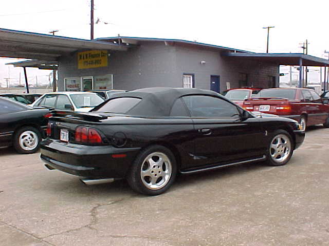 Black Ford Mustang convertible, top up, rear 3/4 view in a car lot