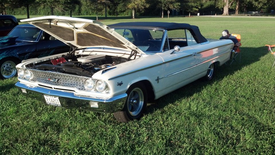 White 1963 Ford Galaxie convertible with hood open, parked on grass next to another car
