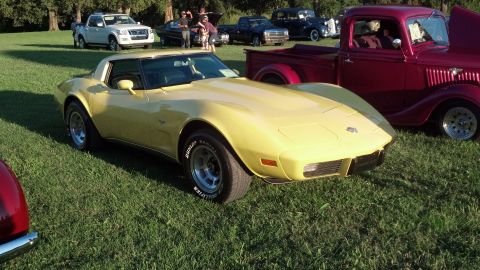 2007 Ford Mustang - A yellow Corvette is parked on grass at an outdoor car show, with other vehicles visible in the background.