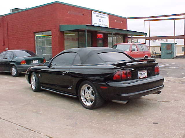 Black Mustang convertible, top up, rear 3/4 view in a parking lot