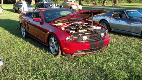 2007 Ford Mustang - A red convertible with black racing stripes is parked on grass with its hood open, alongside other vehicles.
