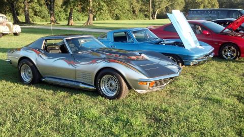 2007 Ford Mustang - A silver 1970s Corvette with custom flame decals is parked on a grassy field alongside other vehicles.