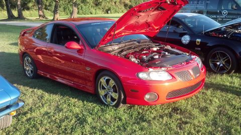 2007 Ford Mustang - Red Pontiac GTO at a car show, hood open, parked next to other vehicles.
