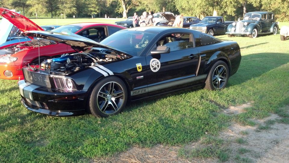 Black 2007 Ford Mustang Shelby GT500 with racing stripes and hood open. Other cars are parked nearby