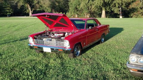 2007 Ford Mustang - A red 1966 Chevrolet Nova coupe is displayed with its hood open, parked next to another vehicle on a grassy field.