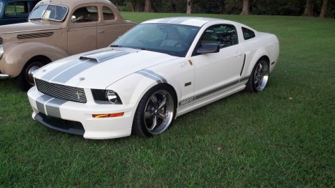 2007 Ford Mustang - A white 2007 Ford Mustang Shelby GT500 is parked on grass next to an older tan car.