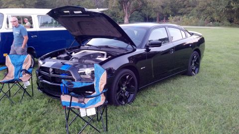 2007 Ford Mustang - A black Dodge Charger is displayed with its hood open, parked next to a blue van at an outdoor event.