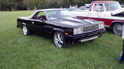 2007 Ford Mustang - Black El Camino with custom wheels and hood scoop sits on grass next to a pickup truck.