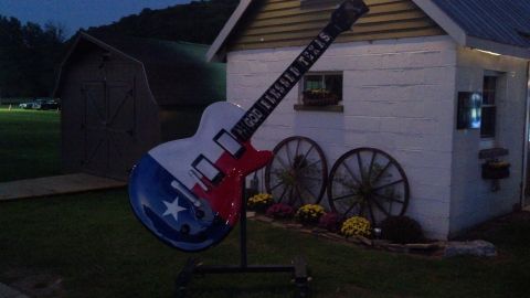 2007 Ford Mustang - A large guitar statue painted with the Texas flag stands outside a building, with wagon wheels and flowers nearby.