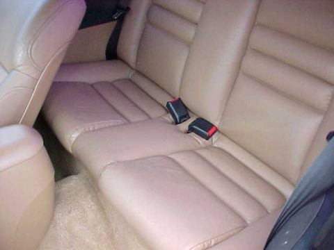 1995 Ford Mustang - Interior view of a car's back seat, showing tan leather upholstery and seatbelts.