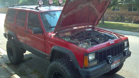 1995 Jeep Cherokee - A red 1995 Jeep Cherokee is parked with its hood up, revealing the engine and modified suspension.