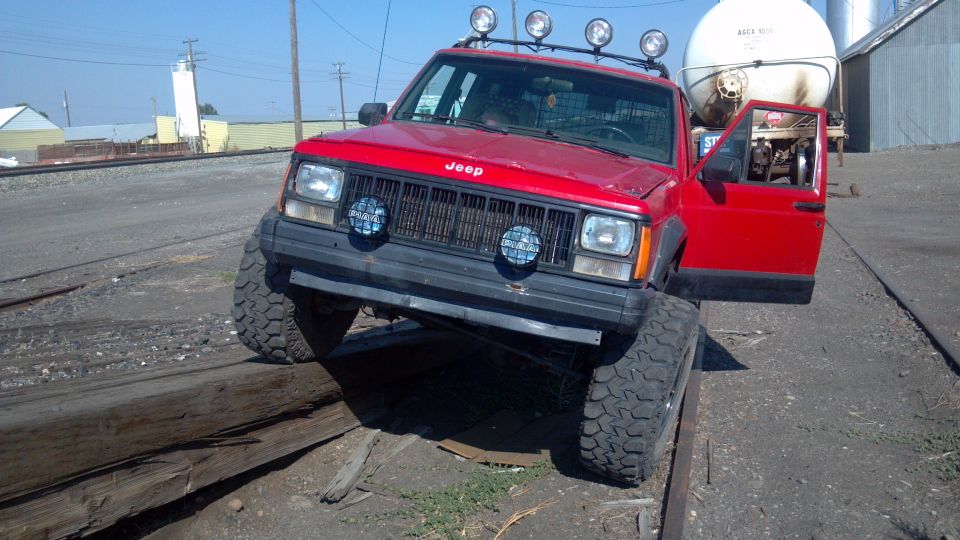 1995 Jeep Cherokee with lifted suspension and off-road tires on railroad tracks, driver's door open