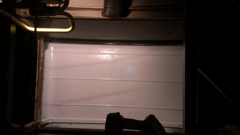 1978 Ford Bronco - The interior of a white garage door is visible, with horizontal paneling and a bright light overhead.