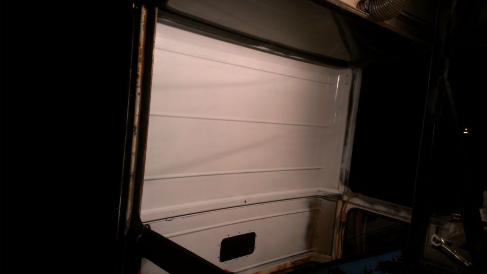 Interior view of a vehicle with white paneled walls and a black vent