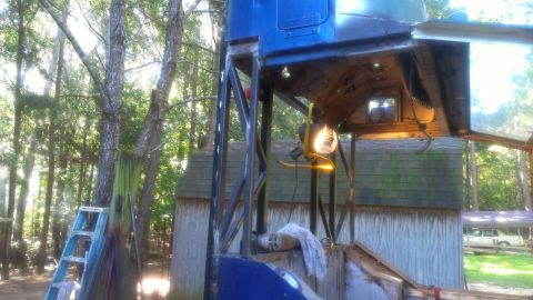 1978 Ford Bronco - A vehicle is undergoing repairs outdoors, elevated on a metal structure with a work light illuminating the underside.