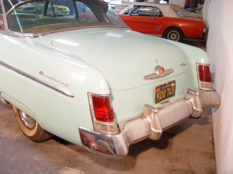 1954 Mercury Monterey - Rear view of a light blue 1954 Mercury Monterey, showing its distinctive tail lights and chrome bumper. Another car is visible in the backg…