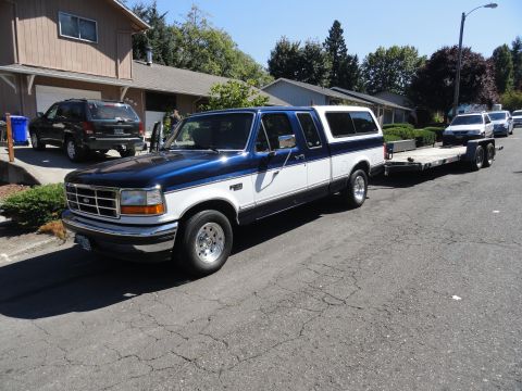 1966 International Scout 800 - A two-tone blue and white Ford F-150 pickup truck, likely from the mid-1990s, is seen towing a car on a trailer.