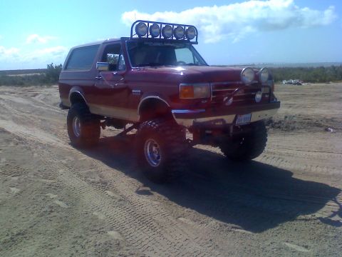 1990 Ford Bronco - This lifted 1990 Ford Bronco is equipped with multiple off-road lights and appears to be on a sandy terrain.