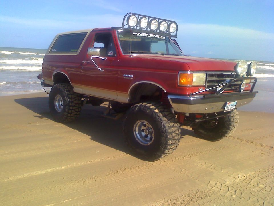Red lifted Ford Bronco with off-road lights and tires on a sandy beach