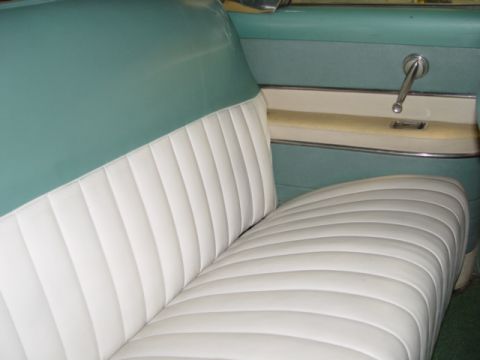 1954 Mercury Monterey - Interior view of a vintage car's white pleated seat and teal door panel with a chrome window crank.