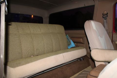 1990 Ford Bronco - The interior of a vehicle shows a bench seat and a passenger seat, with a blue pillow on the bench.