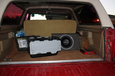 1990 Ford Bronco - The cargo area of an SUV contains audio equipment and storage bins, with a view of the sunset through the tinted rear windows.