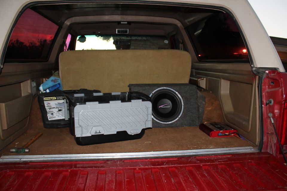 Cargo area of a red and white SUV with a subwoofer, amplifier, and storage bins