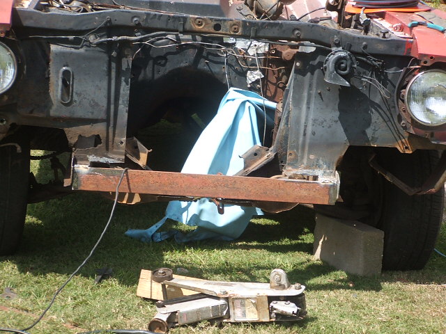 Rusty front end of a red vehicle under construction, showing exposed engine bay and frame