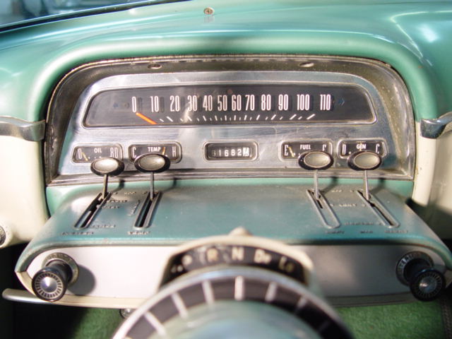 Vintage teal car dashboard with speedometer, gauges, and chrome control levers