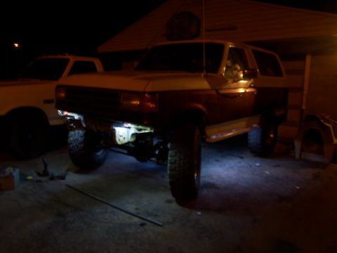 1989 Ford Bronco - A two-tone Ford Bronco is parked in a driveway at night, with another vehicle visible behind it.