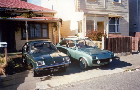 1969 Lincoln Continental - Two vintage hatchbacks parked on a street in front of houses. The car on the left has license plate IR 7277.