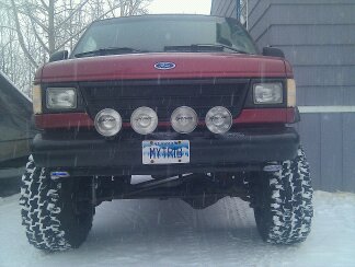 1994 Ford E350 - A red Ford van equipped with large tires and auxiliary lights is parked outside in snowy conditions.