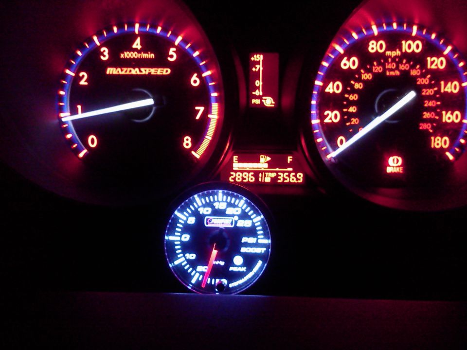 Mazda instrument cluster glowing red with aftermarket blue boost gauge below